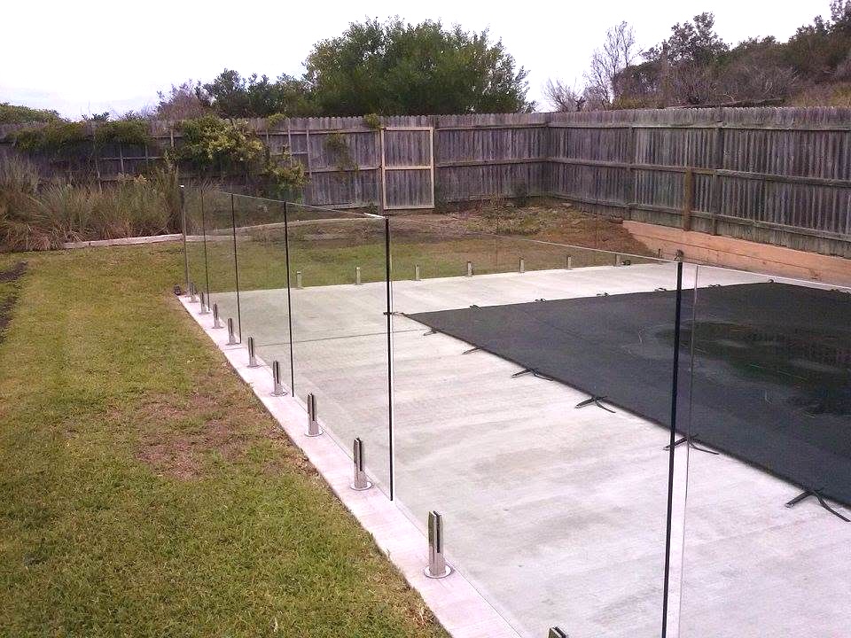 Frameless glass pool fence on spigots enclosing a covered backyard pool