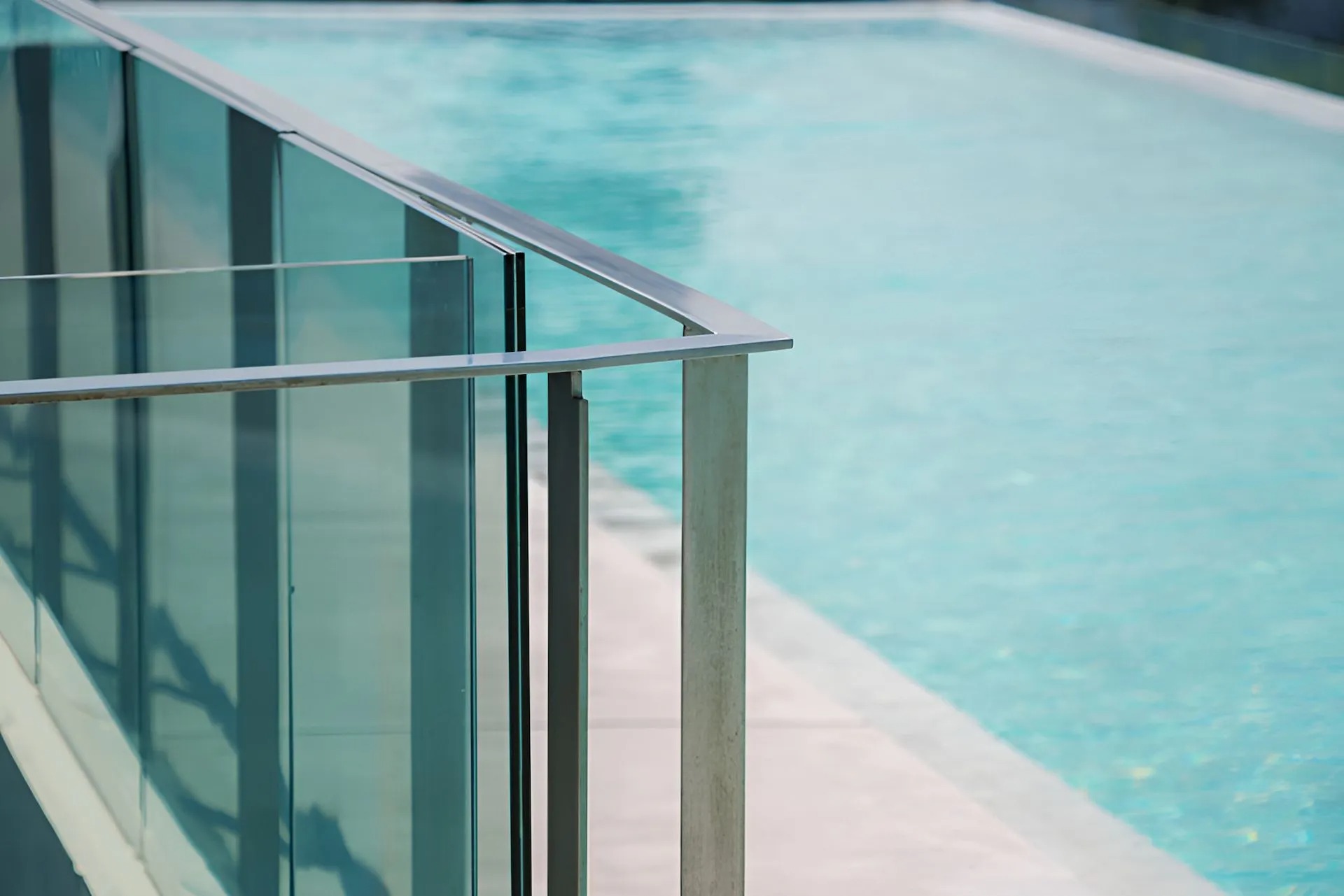 Frameless glass pool fencing with a stainless top rail beside a swimming pool